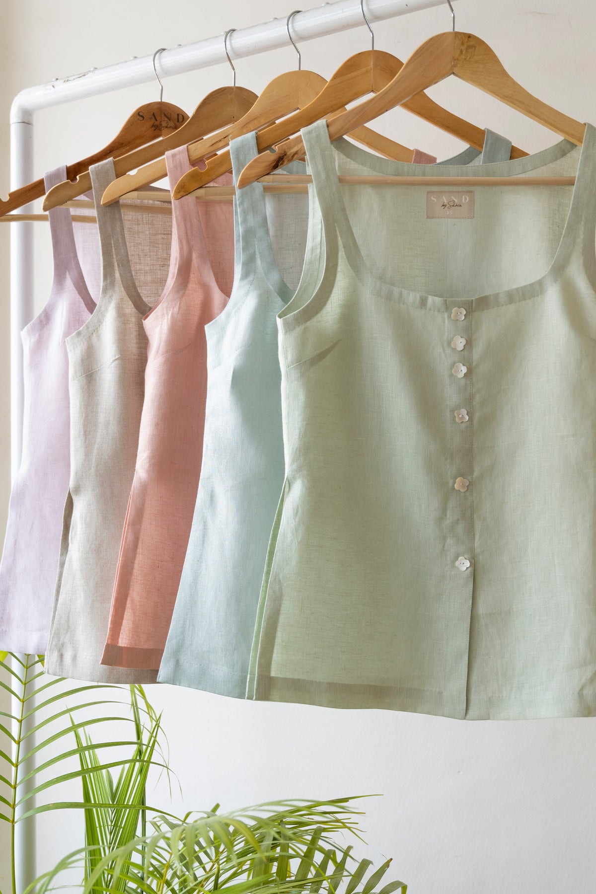 Pastel linen sleeveless tops displayed on wooden hangers