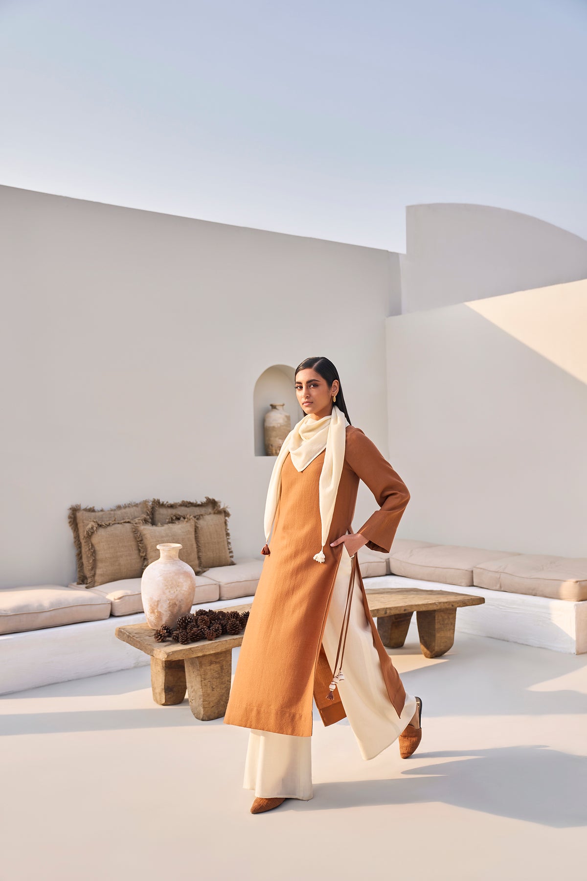 Woman wearing a rust orange tunic dress with white wide-leg pants and scarf