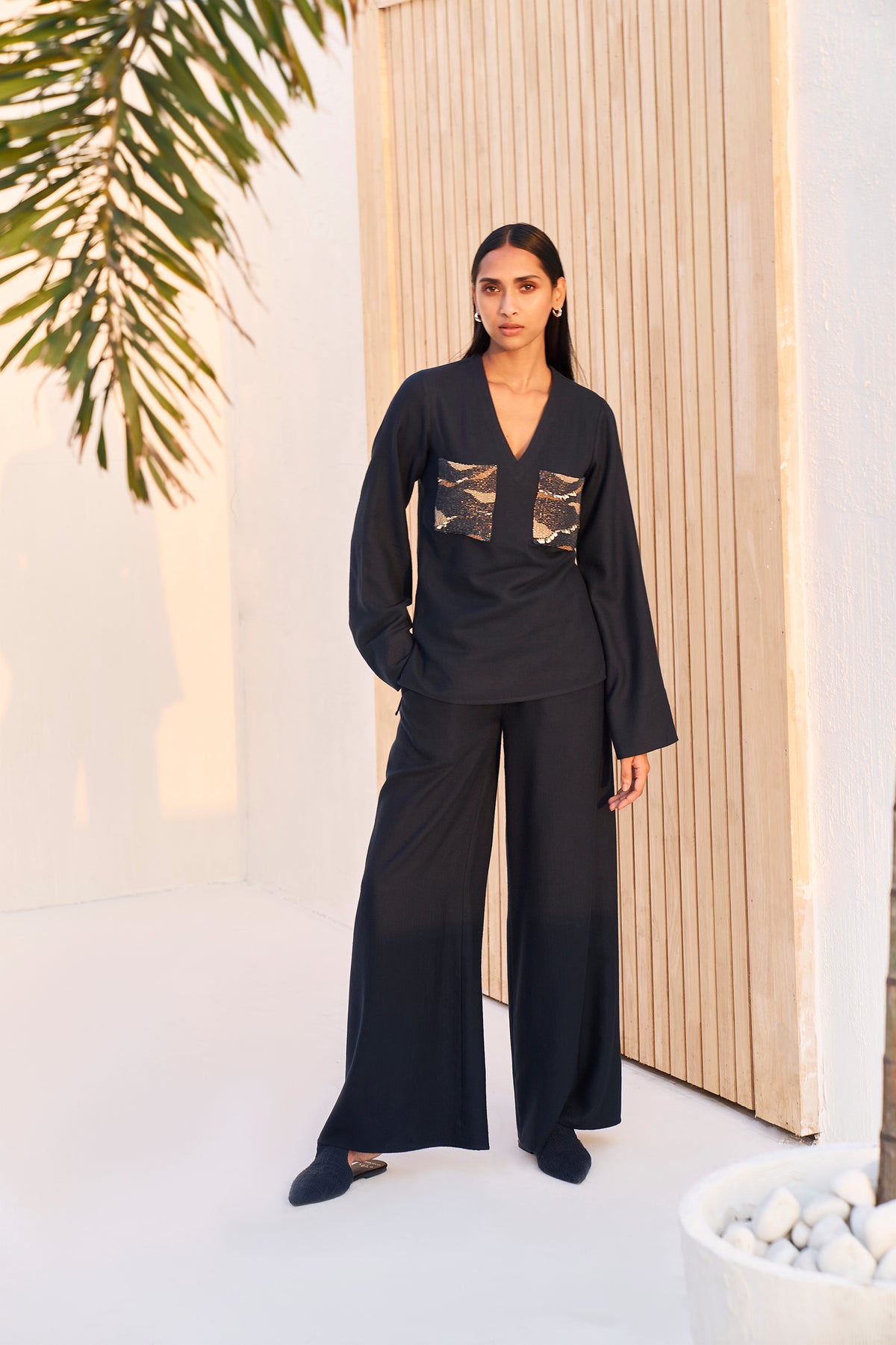 Woman wearing a black V-neck top with wide-leg pants and patterned pockets